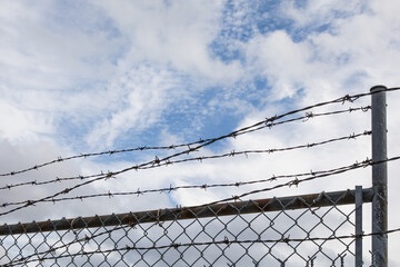 barbed wire topping a chain link fence on a cloudy sky