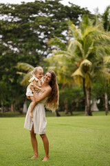 Happy family mother and bchild hugging in a meadow yellow flowers on nature in summer, smiling and look at the camera.