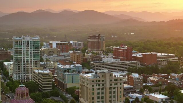 Asheville city in North Carolina at sunset. Downtown architecture with high buildings and Appalachian mountain hills in distance at bright evening. USA travel destination