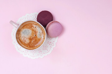 Cup of coffee with macarons on pink background from above