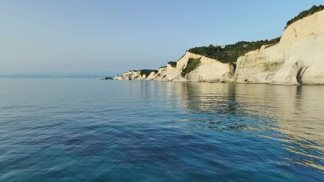 Sunlit cliffs of Corfu Island against the serene Ionian Sea at golden hour, wide shot