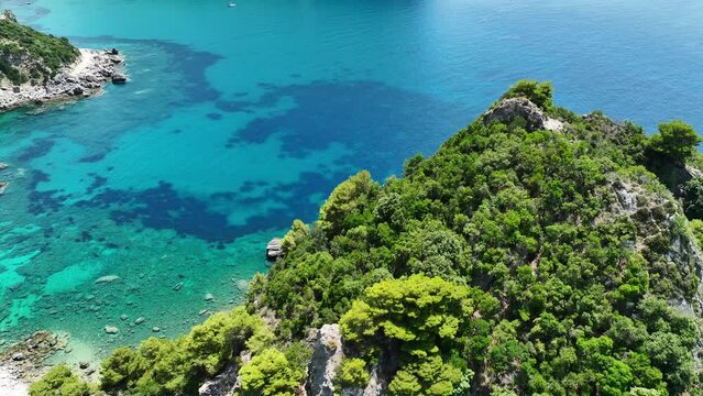 Lush green cliffs on corfu island with crystal blue ionian sea waters, aerial view