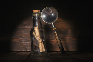 Message scroll letter in the bottle and magnifying glass on the wooden desk tablebackground  front...