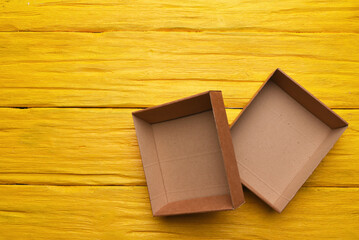 Open empty cardboard boxes on the yellow wooden flat lay desk table background.