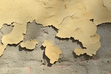 A wall with old yellow paint. The paint is coming off the cement.