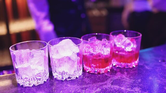 Bartender working, beautiful row line of different coloured liquor alcohol cocktails on a party in a bar, and others on catering banquet on event, barman mixing drinks and beverages in a club
