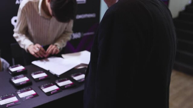 Process of checking in on a conference congress forum event, registration desk table, visitors and attendees receiving a name badge and entrance wristband bracelet and register electronic ticket
