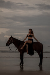 Young long hair woman in black drss is  riding  horse on seascape background. Rider female drives...