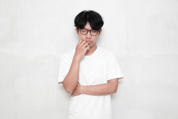 Young Asian man wearing t-shirt and glasses on white background thinking looking tired and bored with problems