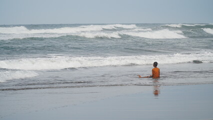 The boy was sitting on the beach waiting for the waves to come