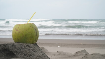 Coconut fruit with straw on beach sand. Blur sand and waves background. Focus selected