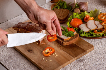 Hands of young man making sandwiches with smoked lard and cutting meat and vegetables for serving....