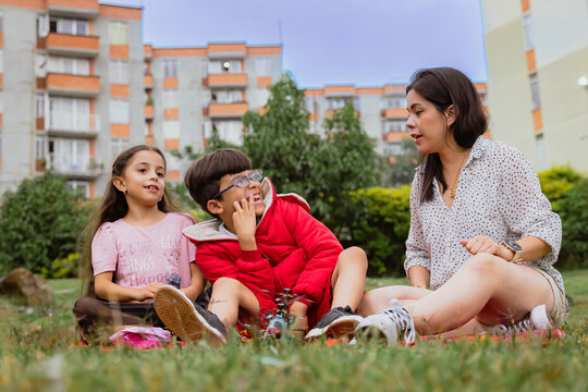 International Children Day. Latin mother having fun with her young children outdoors. Sitting on the ground playing with their hands. Concept of family. Single mother with two young children.