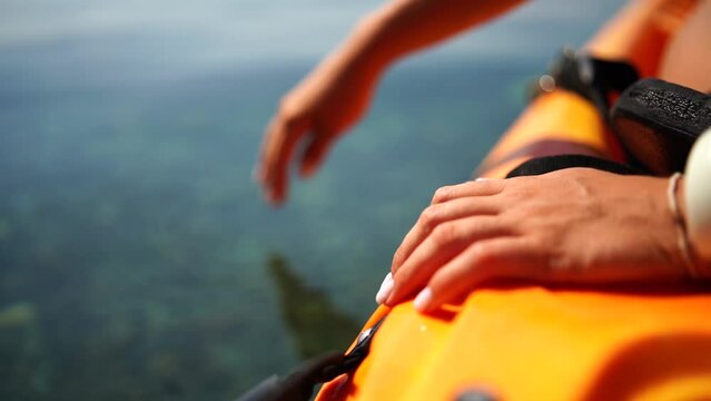 A person is touching the water with their hand. The water is clear and calm. The person is wearing a yellow life jacket.