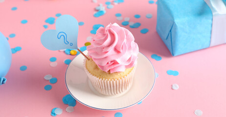Delicious cupcake with question mark, gift box and decorations on pink background. Gender reveal party concept