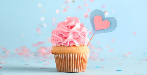 Delicious cupcake with pink frosting and decor on blue background. Gender reveal party concept