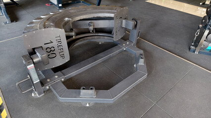 A black tire flip machine designed for heavy lifting and strength enhancement showcased inside a spacious gym setting.