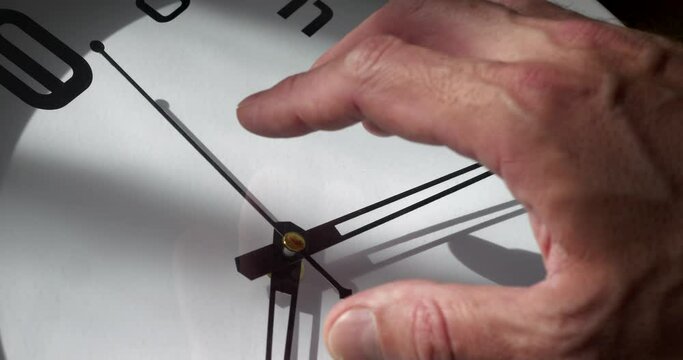 a man's hand over the dial of a large clock, the concept of the irrevocable flow of time