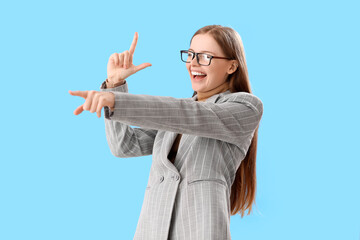 Young businesswoman showing loser gesture and pointing at something on blue background