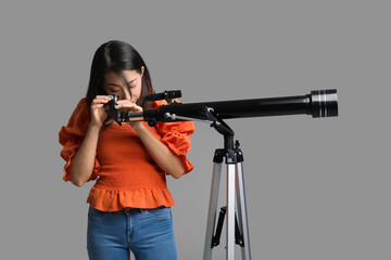 Young Asian woman using telescope on grey background