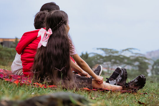 International Children Day. Latin mother having fun with her young children outdoors. Sitting on the ground playing with their hands. Concept of family. Single mother with two young children.