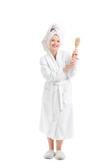 Young woman in bathrobe with massage brush after shower on white background