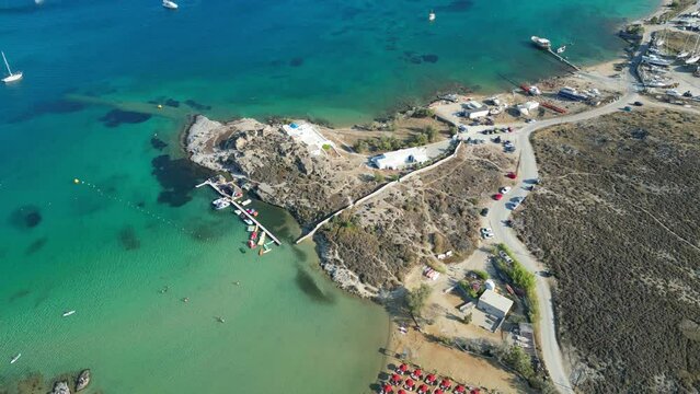 Aerial footage of turquoise waters and a small beach club on the island of Paros, one of the many Cyclades Islands in the Aegean Sea.