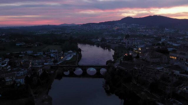 Twilight over Barcelos, with the iconic medieval bridge lit by streetlights reflecting on the C&aacute;vado River. Portugal aerial