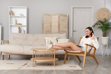 Happy young woman using laptop in wooden armchair at home