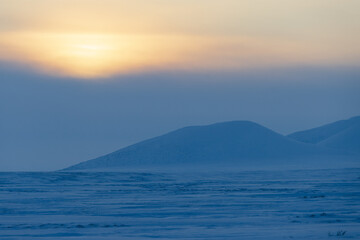Winter arctic landscape. View of the snow-covered tundra and snow-capped mountains. Cold frosty winter weather. Endless Arctic Desert. Northern nature of the polar region. Sunset. Chukotka, Russia.