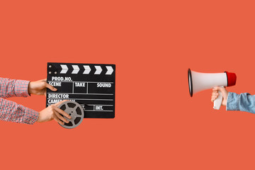 Hands with movie clapper, film reel and megaphone on orange background