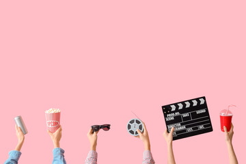 Many hands with bucket of popcorn, movie clapper and drinks on pink background