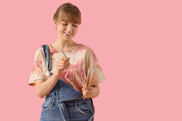 Female artist with paint brushes on pink background