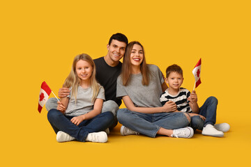 Beautiful family with flags of Canada sitting on yellow background
