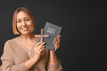 Happy adult woman with Holy Bible and wooden cross on black background