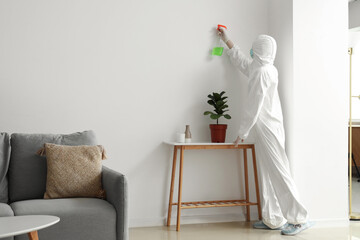 Female worker of cleaning service removing mold from wall in room