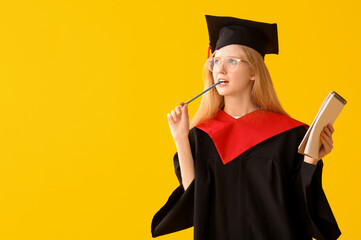 Female graduating student in mortar board with notebook on yellow background