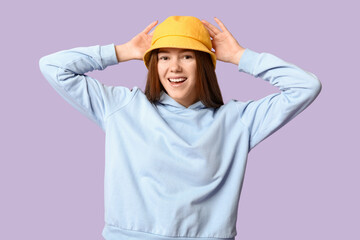 Stylish young girl in hoodie and hat on lilac background