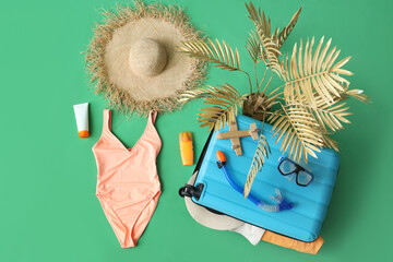 Composition with suitcase, beach accessories, female swimsuit and exotic plant on green background