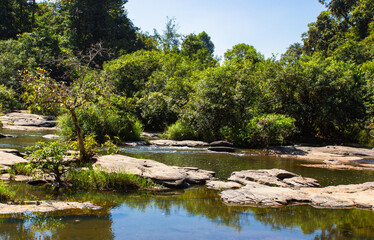 Creek with big stones and forest trees during summer hot season in north--eastern Thailand.