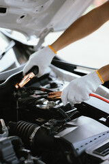 Close-up of auto mechanic charging car battery with electric rail jumper cables	