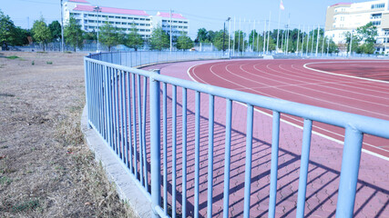 Metal fence around the stadium. Closeup of a steel fence surrounding an outdoor sports stadium with a running track on the background of buildings and blue sky with copy space with selective focus.
