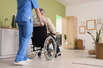 Young caregiver with senior man in wheelchair at home, back view
