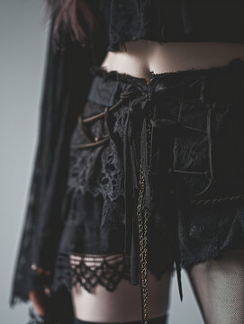 A close-up captures a woman's bare midriff adorned with a gothic-inspired lace mini skirt.