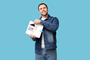 Young man holding purse with credit cards on blue background