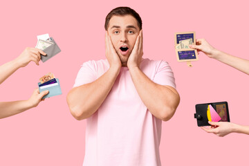 Young shocked man and many female hands holding wallets with credit cards on pink background