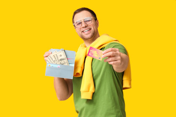 Young happy man in eyeglasses holding purse with money and credit card on yellow background