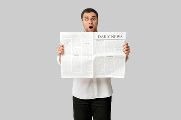 Shocked young man with newspaper on white background