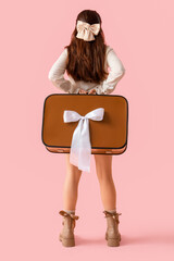 Stylish young woman with bows and suitcase on pink background