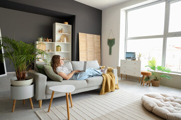 Young woman using laptop on grey sofa at home